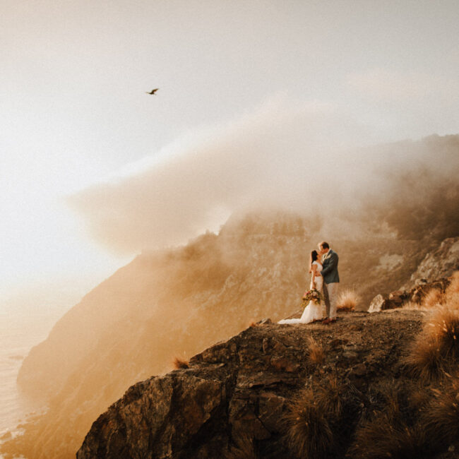 Elopement couple kissing on cliff in Big Sur during sunset