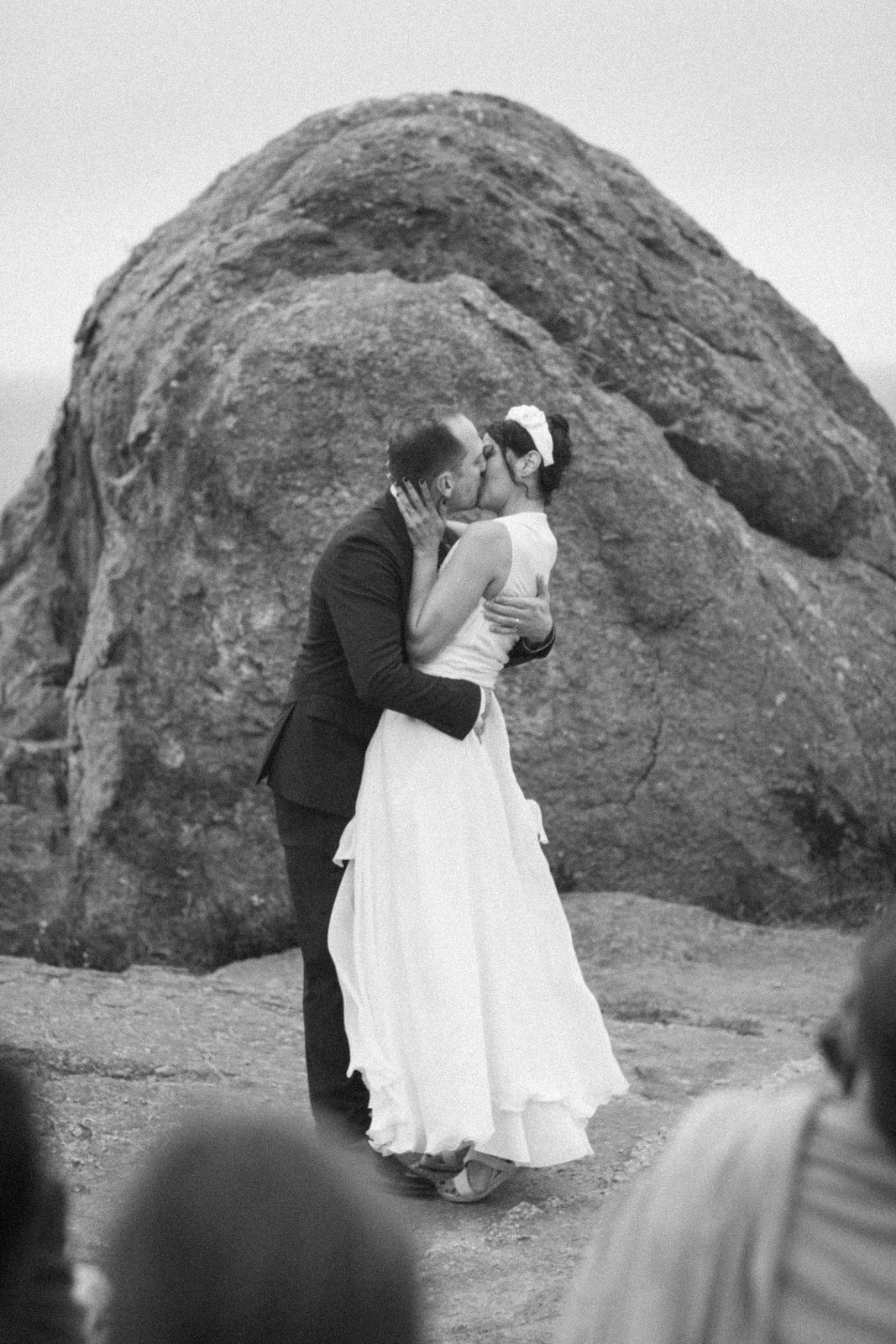 Couple kissing in front of large rock on their wedding day