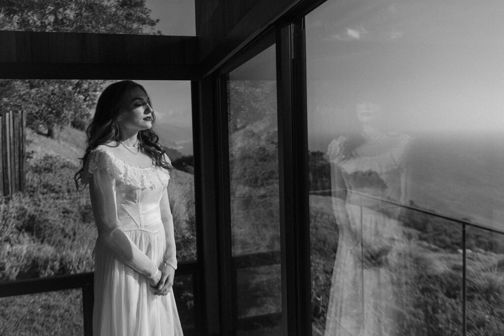 Bride looks out the window at the Big Sur coast in her vintage wedding dress